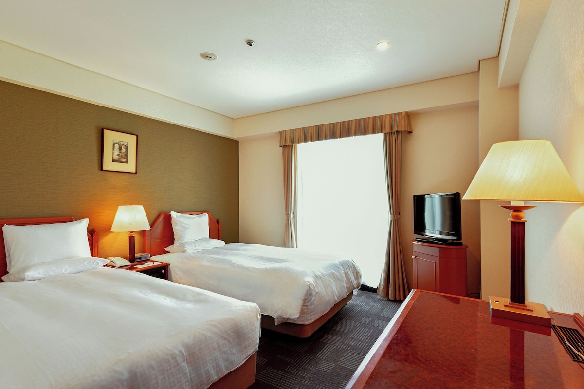 Habitación de hotel con dos camas, televisión, escritorio y lámpara.