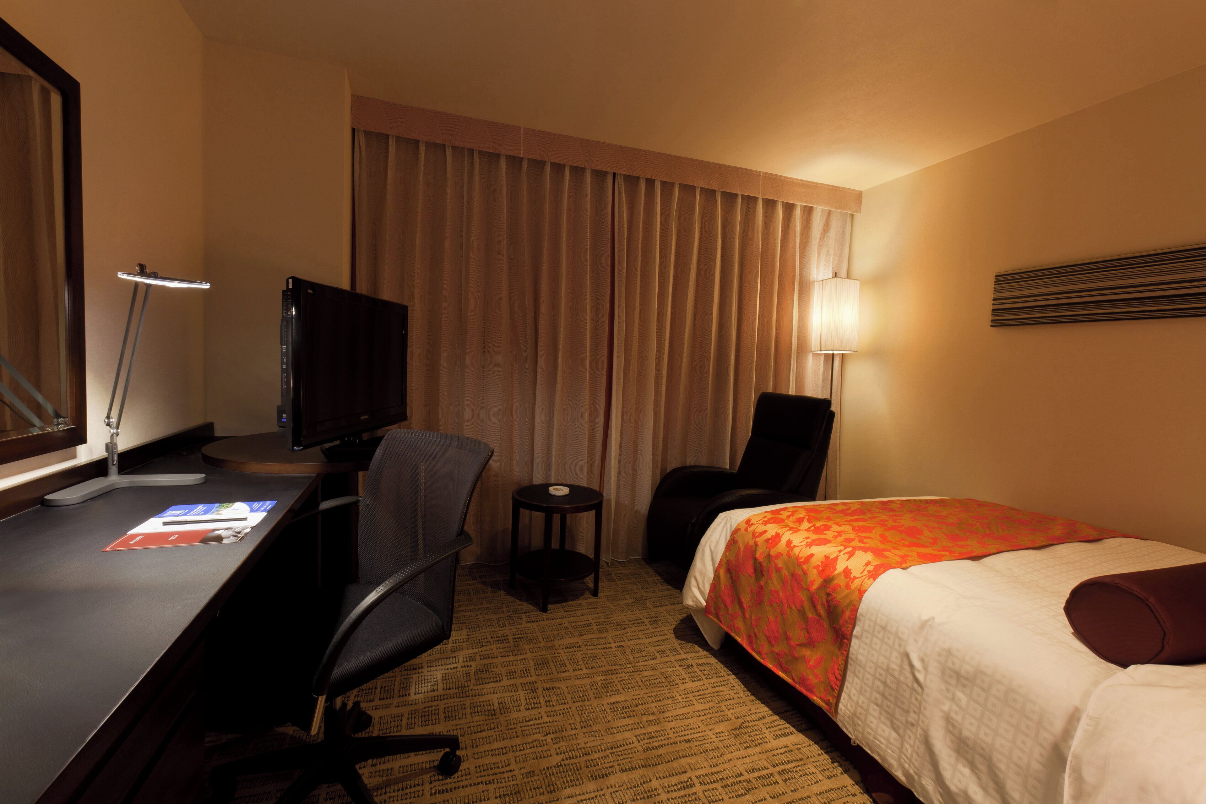 Ein Hotelzimmer mit Schreibtisch, Stuhl, Bett und Fernseher.