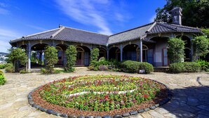 A traditional building with a tiled roof, arched windows, and a landscaped garden with a circular flower bed. - Crowne Plaza ANA Nagasaki Gloverhill by IHG (Nagasaki)
