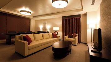 A hotel room with a sofa, a coffee table, a TV, and a dining area with chairs and a table.