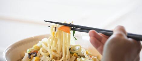 A bowl of noodles with vegetables and corn being lifted with chopsticks.