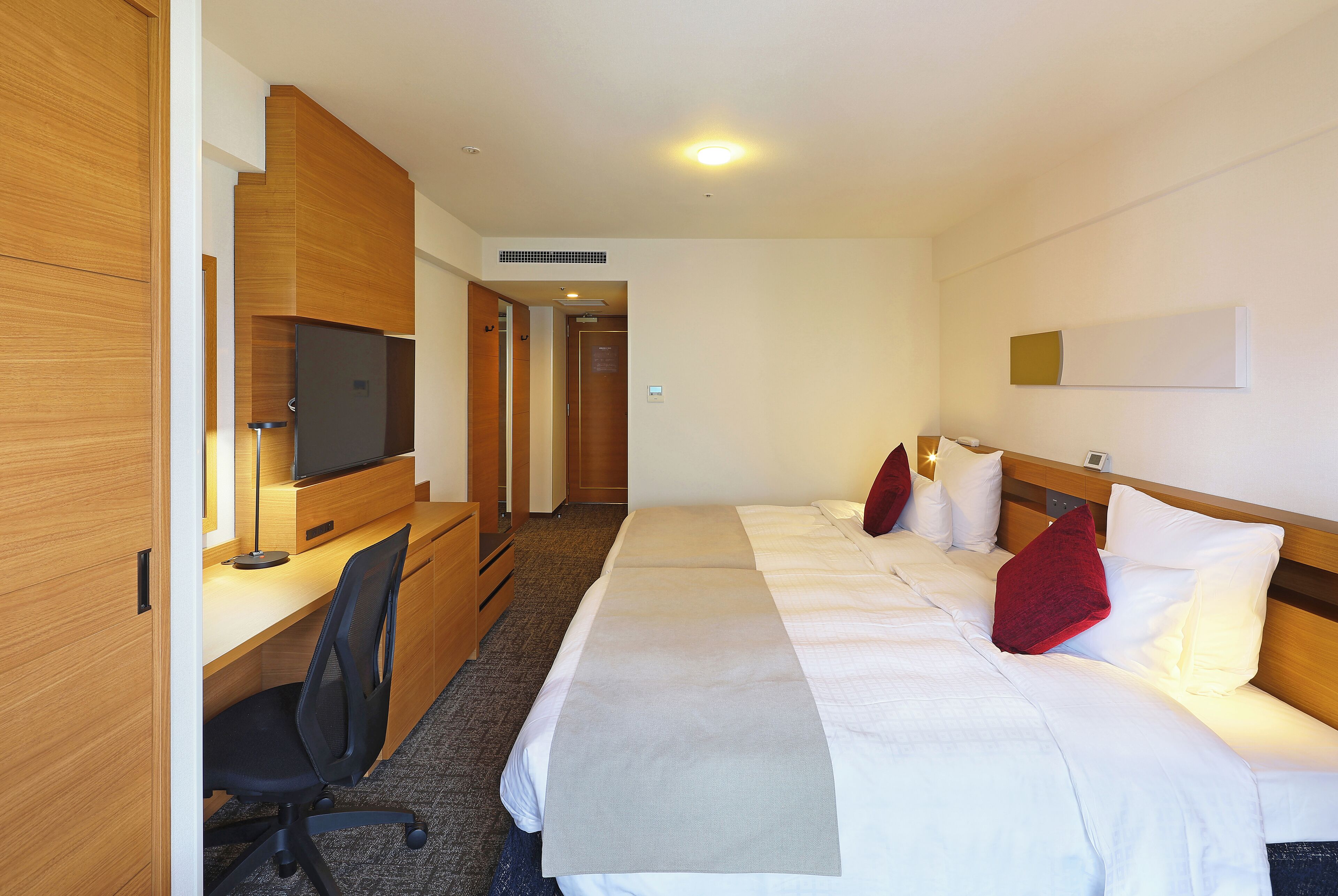 A hotel room with a bed, a desk, a chair, and a television.