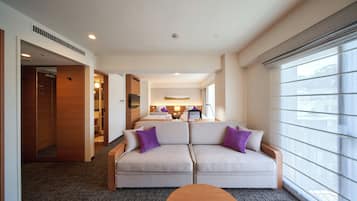 Una habitación de hotel con sofá, una mesita redonda, cama y ventana con persianas.