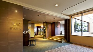 A hotel lobby with a reception desk, a staircase, and a large window offering a view of the outdoors. - Crowne Plaza ANA Nagasaki Gloverhill by IHG (Nagasaki)