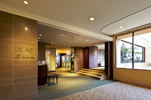 Un vestíbulo de hotel con un mostrador de recepción, una escalera y un ventanal que ofrece vistas al exterior.