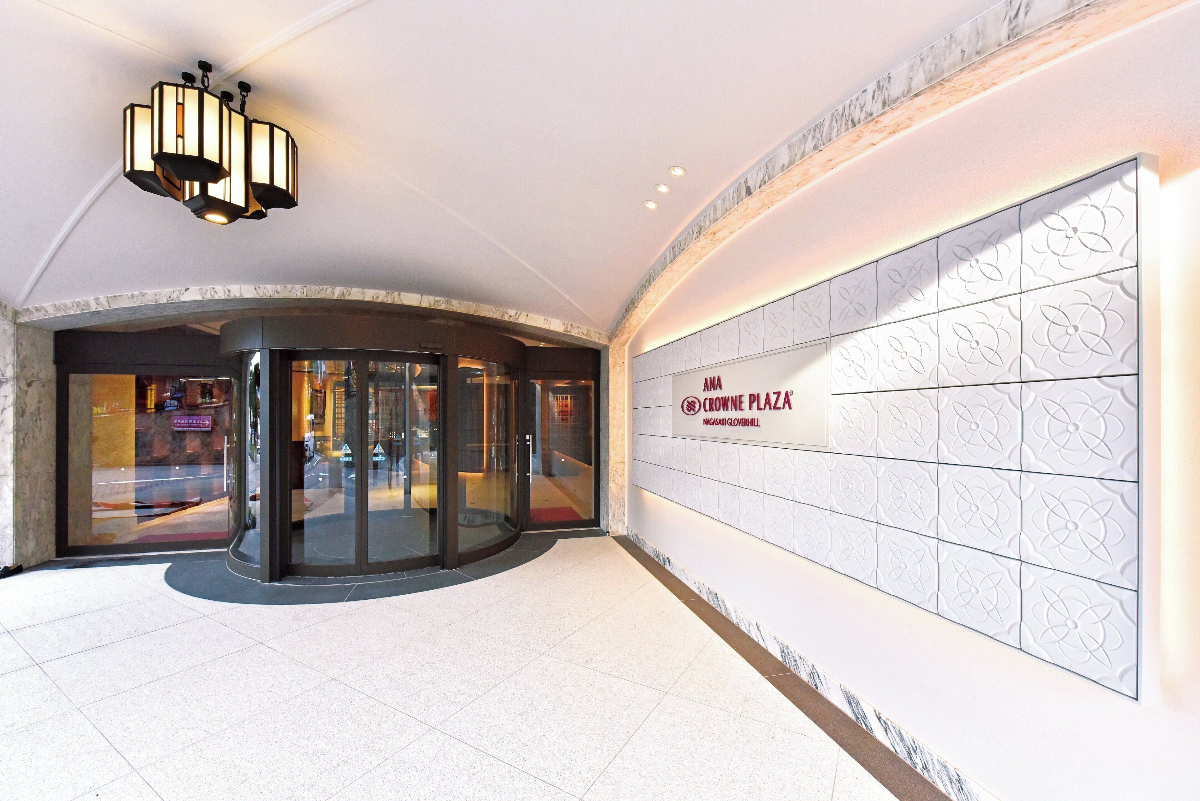 A modern entrance with a revolving door, a glass facade, and a wall with a floral pattern.