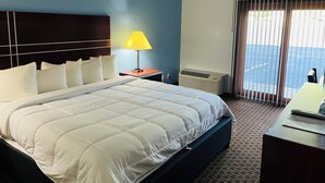 A hotel room with a large bed, a bedside table with a lamp, an air conditioning unit, and a view of the sea through the window.