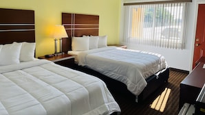 A hotel room with two beds, a wooden headboard, a nightstand with a lamp, and a window with blinds.