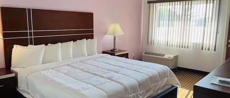 Une chambre d’hôtel avec un grand lit, une table de chevet avec une lampe, une fenêtre avec des stores et un climatiseur fixé au mur.