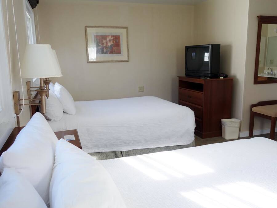 Ein Hotelzimmer mit zwei Betten, einem Fernseher auf einem Holzständer, einem Schreibtisch und einem Spiegel.