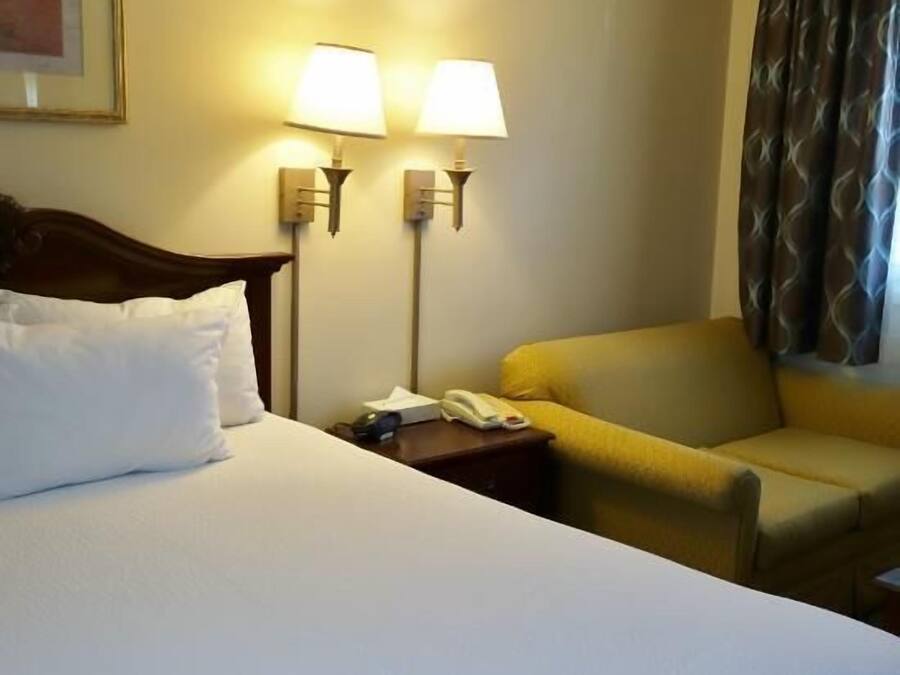 A hotel room with a large bed, two bedside lamps, a small table, a chair, and a window with curtains.