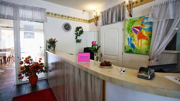 Un mostrador de recepción con un letrero de bienvenida, un jarrón de flores, un cuadro y una caja registradora.