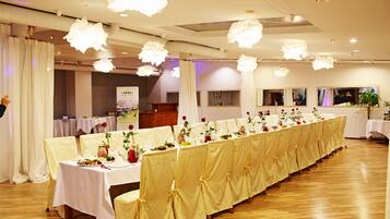 Ein Festsaal mit langen Tischen, bedeckt mit weißen Tischdecken, geschmückt mit floralen Mittelpunkten und roten Rosen.