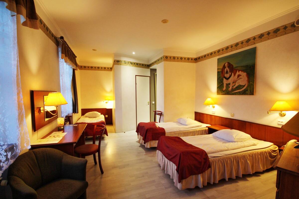 A hotel room with two single beds, a desk with a chair, a small table, and a lamp.