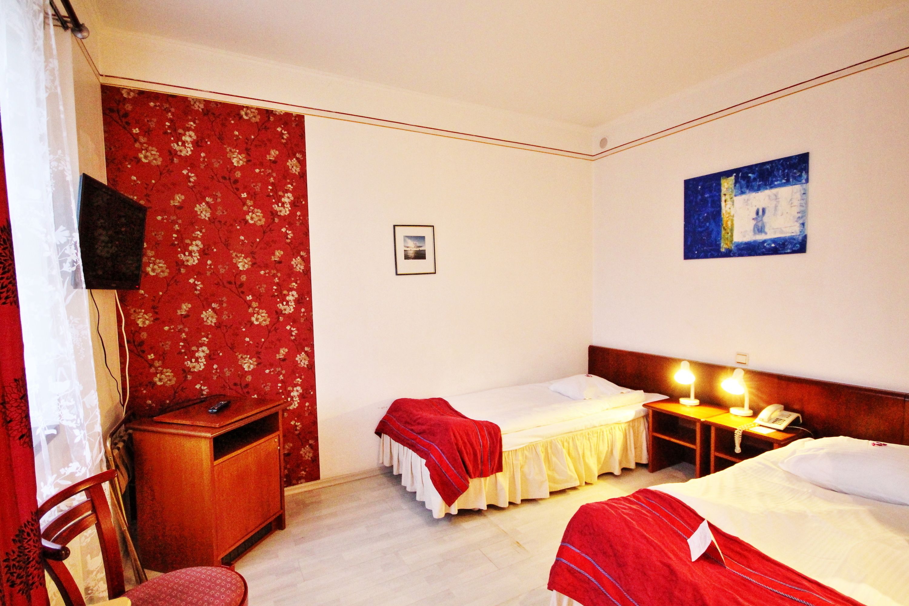 Hotellihuone, jossa on kaksi sänkyä, työpöytä tuolilla, televisio ja yöpöytä lampun kanssa.