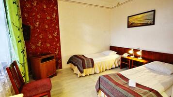 A hotel room with two single beds, a wooden nightstand with a lamp, a desk with a telephone, a chair, and a painting on the wall.