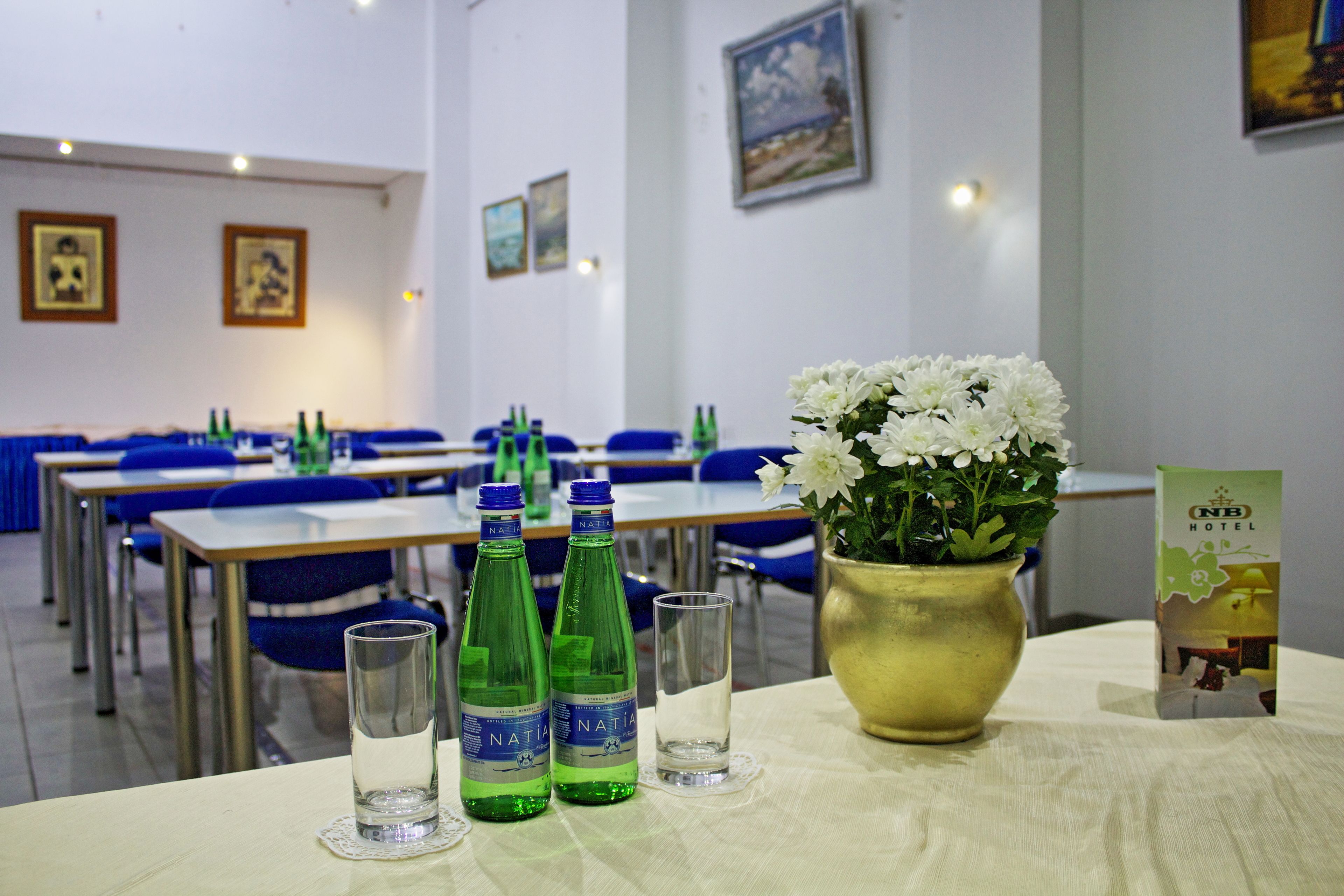 Hotellihuone, jossa on ruokapöytä kahdelle katettuna, kaksi vesipulloa, lasi ja maljakko valkoisia kukkia.