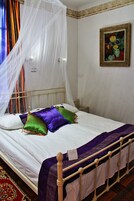 Una cama con sábana blanca, almohadas moradas y verdes, una manta morada y un cabecero de madera.