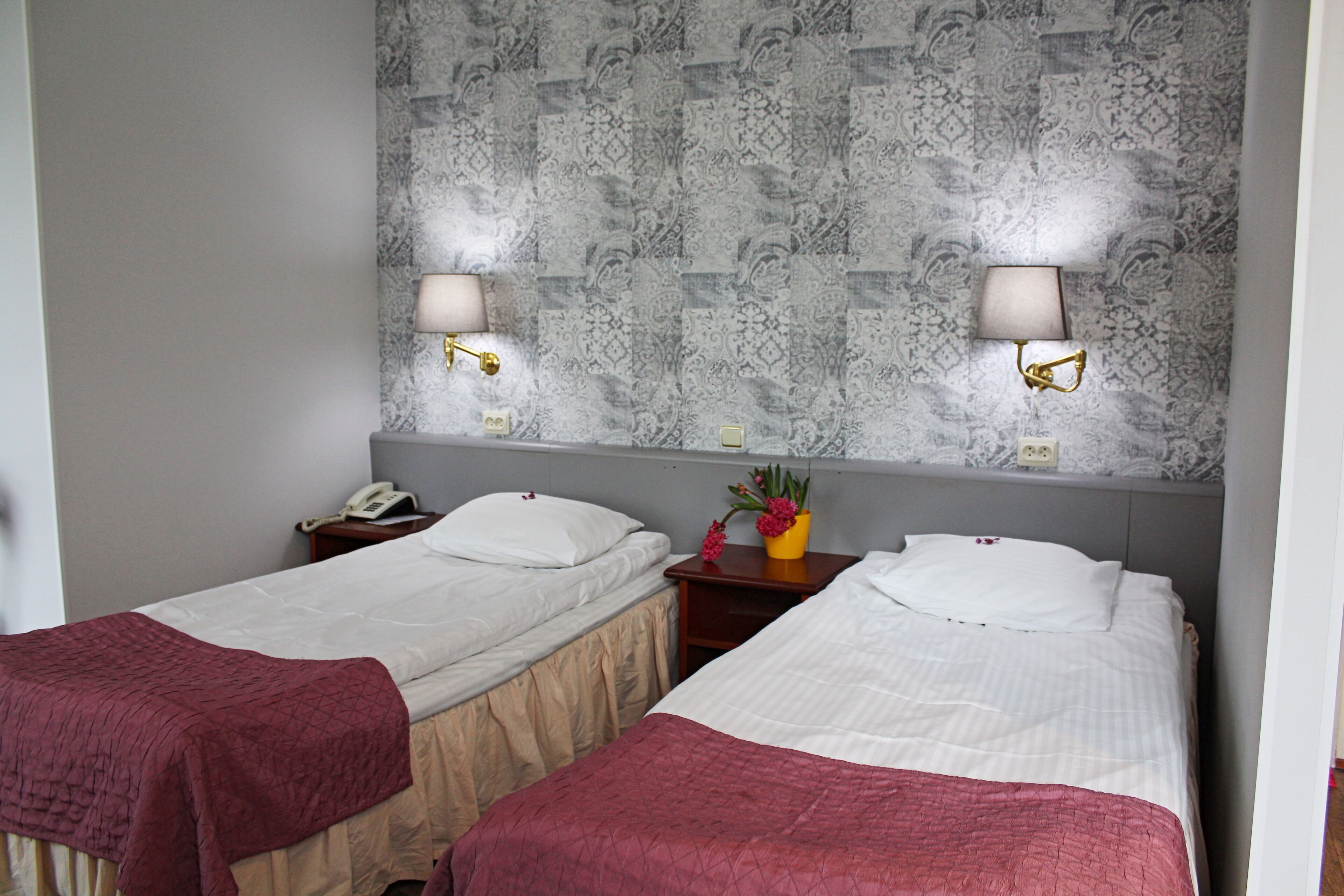 Two single beds with white linens, a nightstand with a telephone, and a wall-mounted lamp.