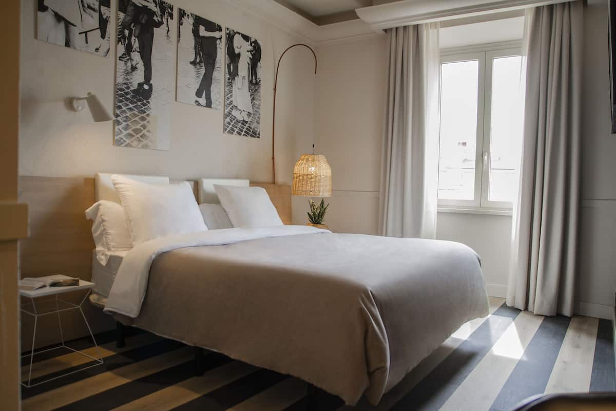 Un lit bien fait, recouvert d’une couvre-lit aux couleurs neutres, une table de chevet avec une lampe et une œuvre d’art accrochée au mur.