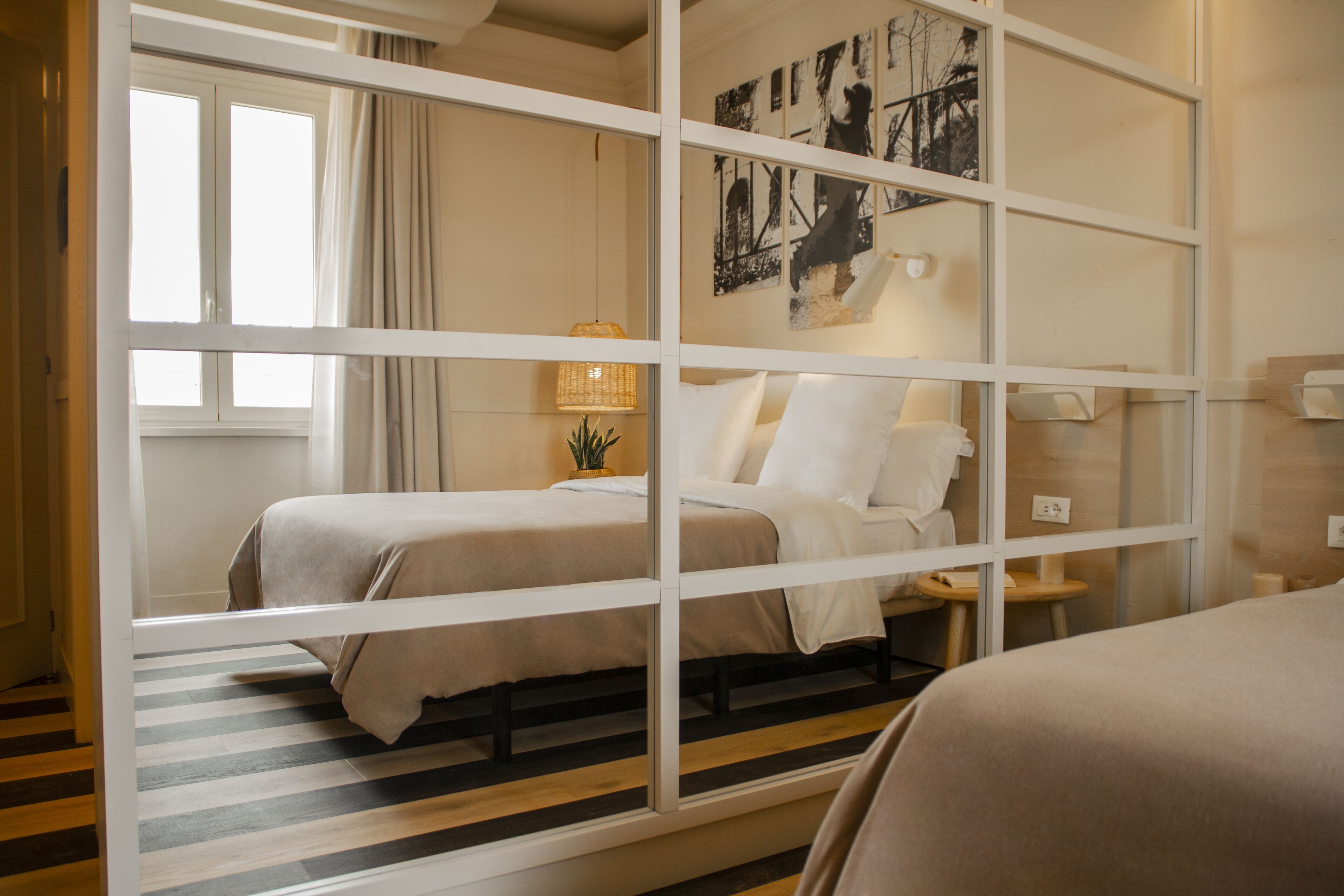 A hotel room with a bed, a bedside table, a lamp, and a window with curtains.