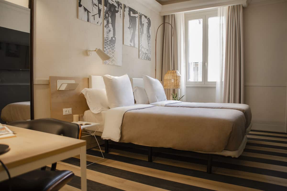 Une chambre d’hôtel avec un lit, un bureau, une chaise, une lampe et des œuvres d’art accrochées au mur.