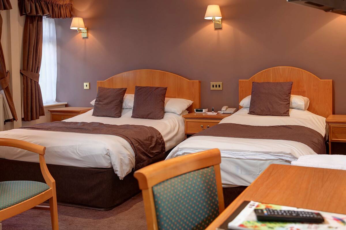 A hotel room with two beds, each with a wooden headboard, a bedside table, and a lamp.