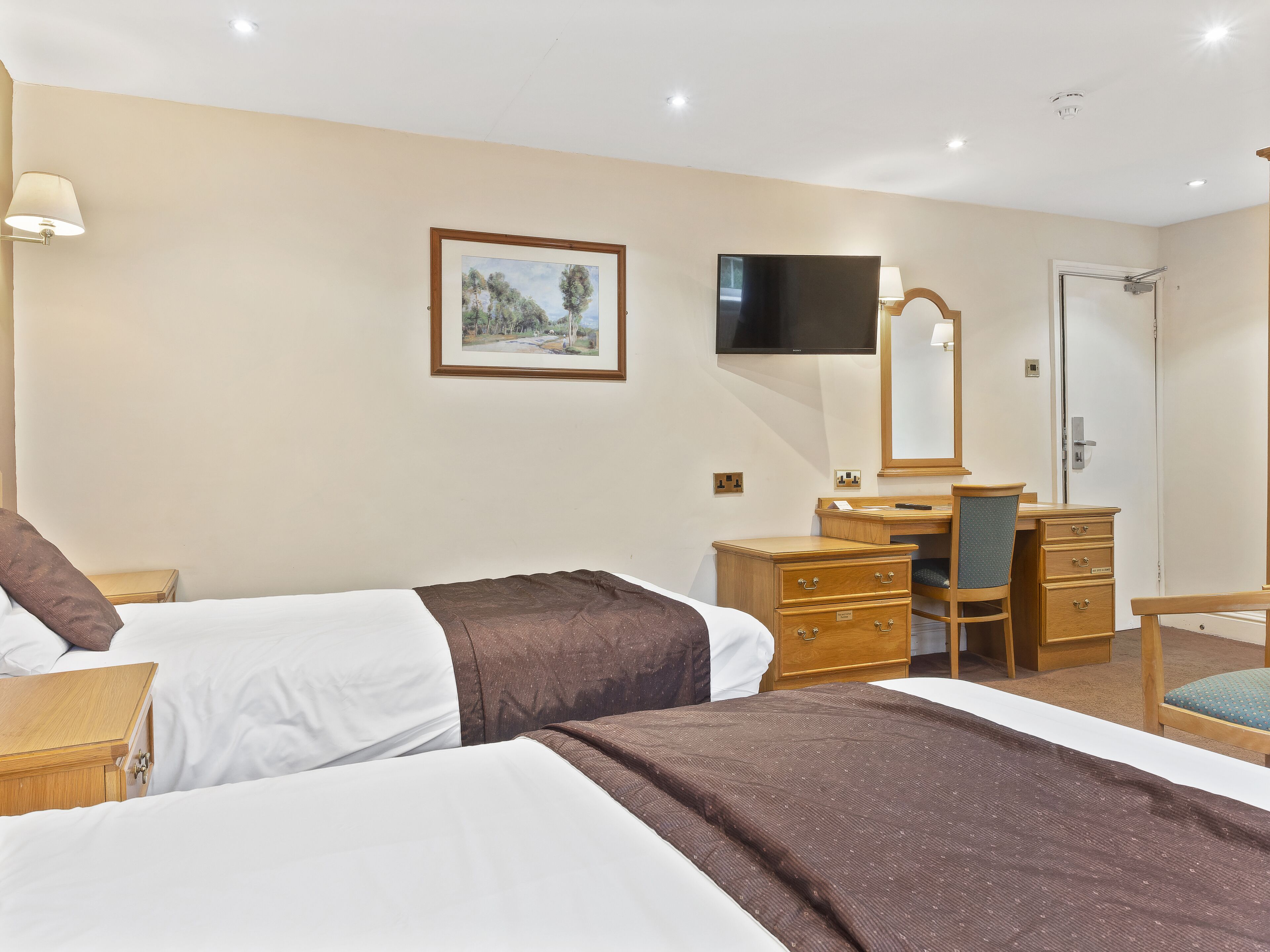 A hotel room with two beds, a desk with a chair, a television, a mirror, and a door.