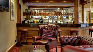 A bar area with leather chairs, a bar counter with multiple taps, and a wooden floor. - The Old Mill Hotel (Bury)