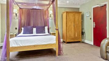 A four-poster canopy bed with a wooden frame and sheer curtains, a wooden wardrobe, and a red door in a hotel room.