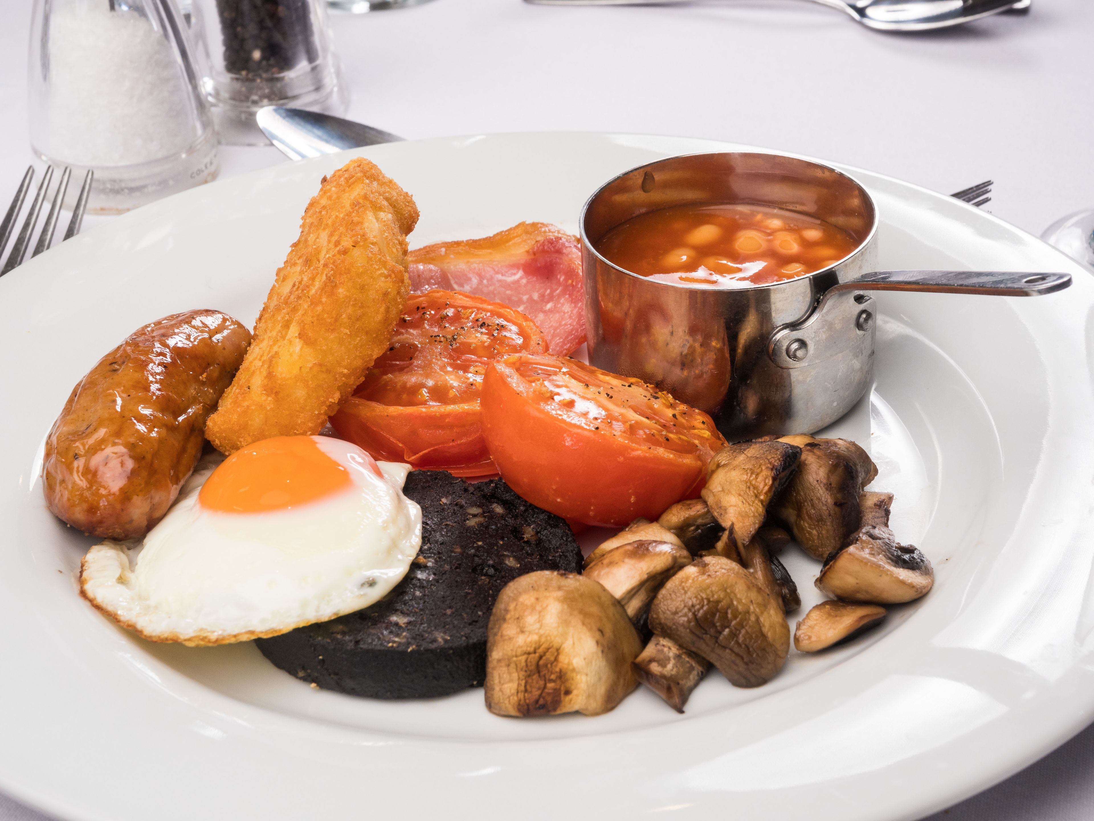 A plate of breakfast food including sausages, eggs, tomatoes, mushrooms, and beans.