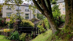 A traditional building with a stone wall, a wooden bridge, and lush greenery. - The Old Mill Hotel (Bury)