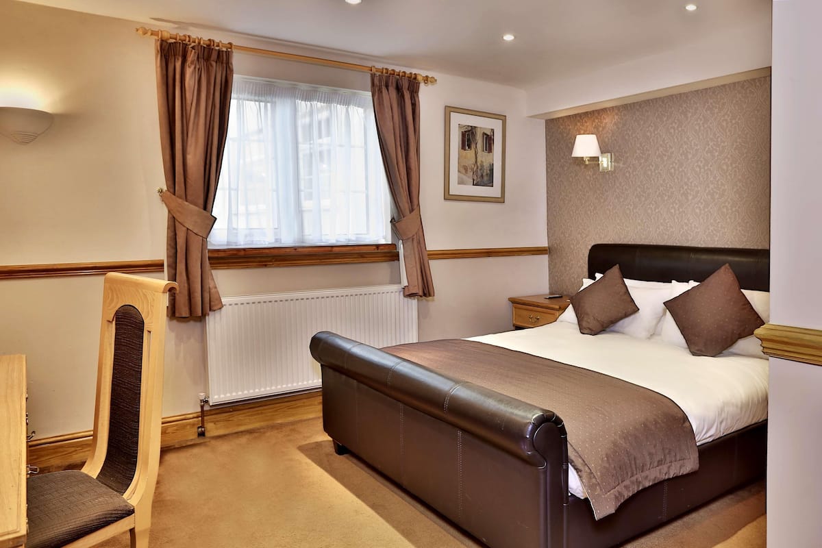 A hotel room with a bed, a chair, a nightstand, a lamp, and a window with curtains.