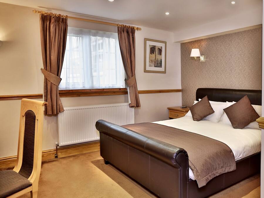 Una habitación de hotel con una cama grande, una silla de madera, una mesita de noche y una lámpara de pared.