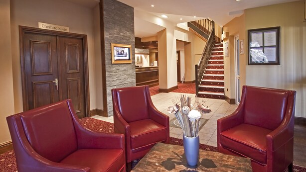 A lobby with red leather chairs, a wooden table, a staircase, and a sign reading "Cheshire Suite". - The Old Mill Hotel (Bury)