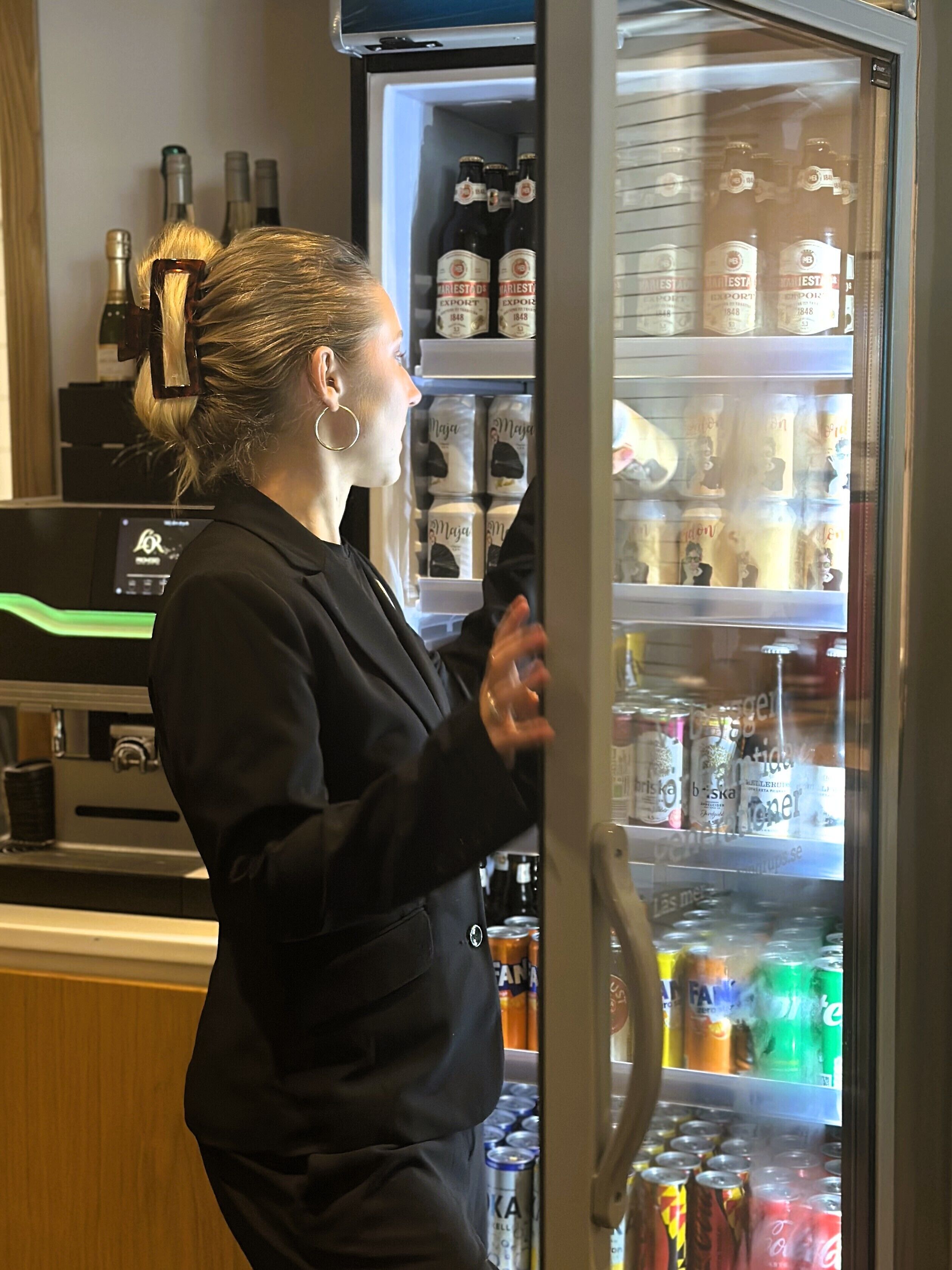 A person in a black uniform opening a refrigerator stocked with beverages and bottles.
