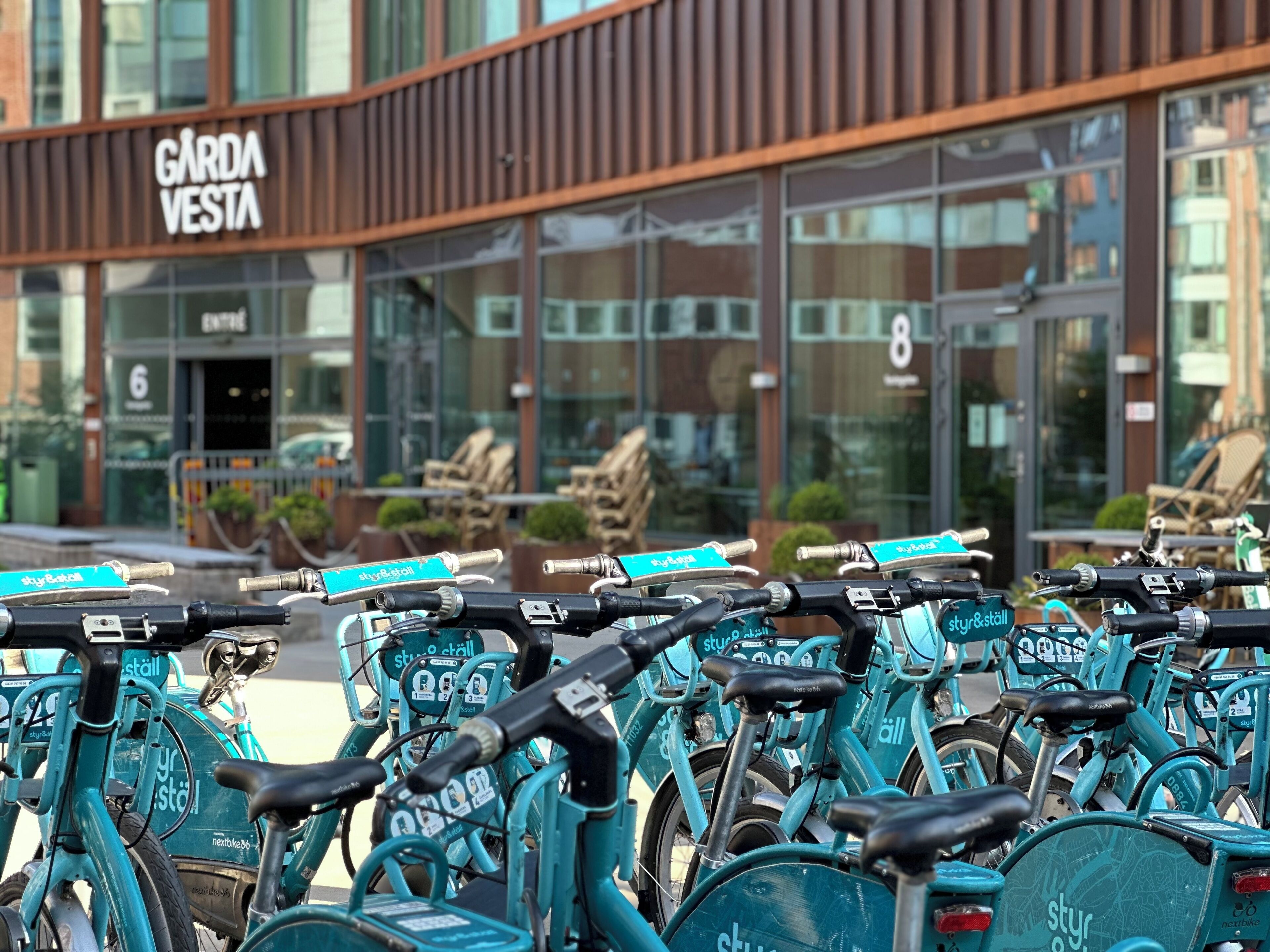 Una fila de bicicletas color turquesa estacionadas frente a un edificio con un letrero que dice "GARDAVESTA".