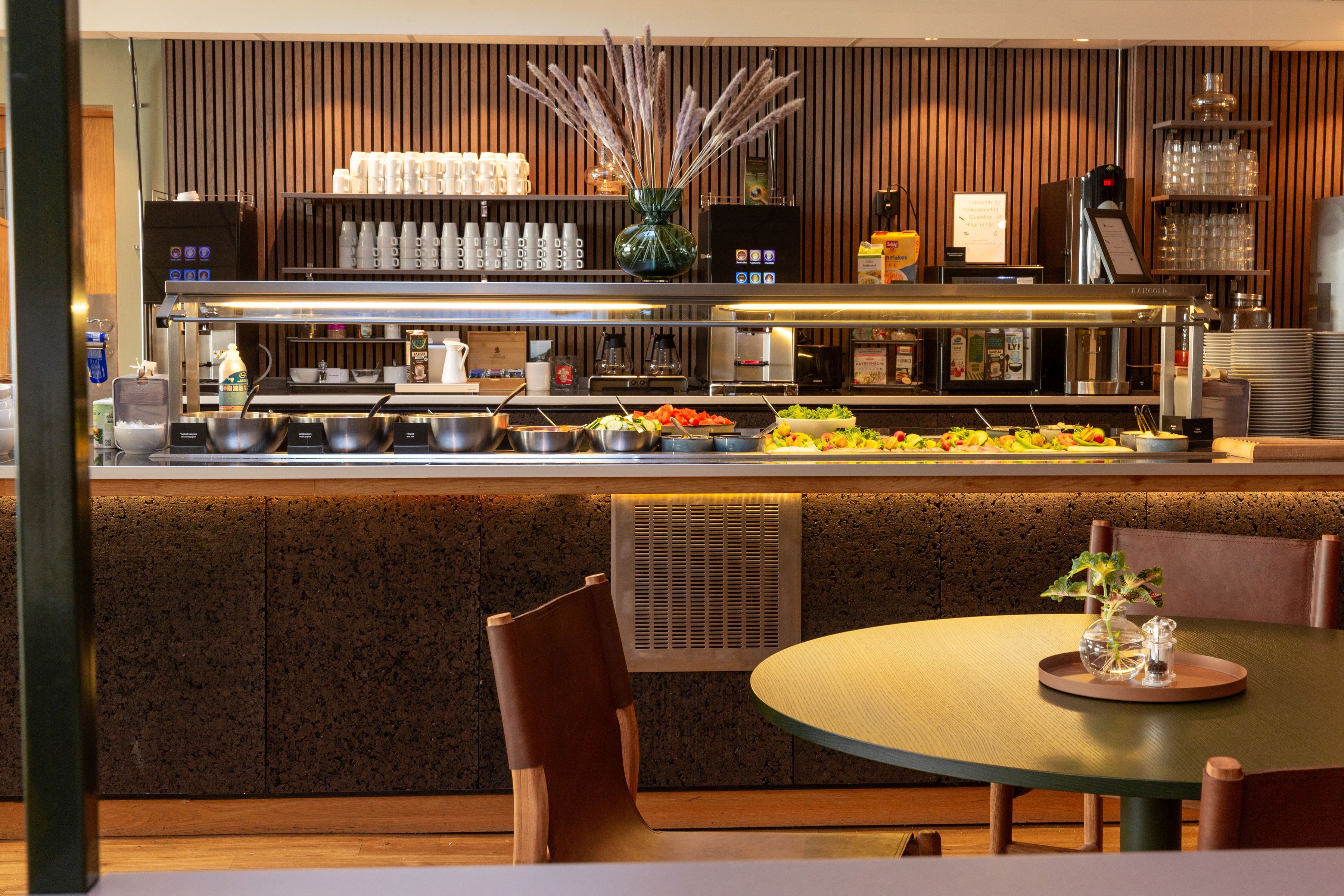 En moderne restaurant med buffetbar, siddepladser og en dekorativ plante i midten.