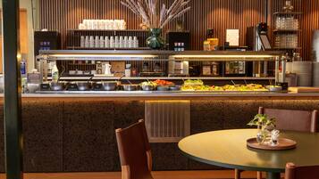 A modern restaurant with a buffet bar, seating area, and a decorative plant centerpiece.