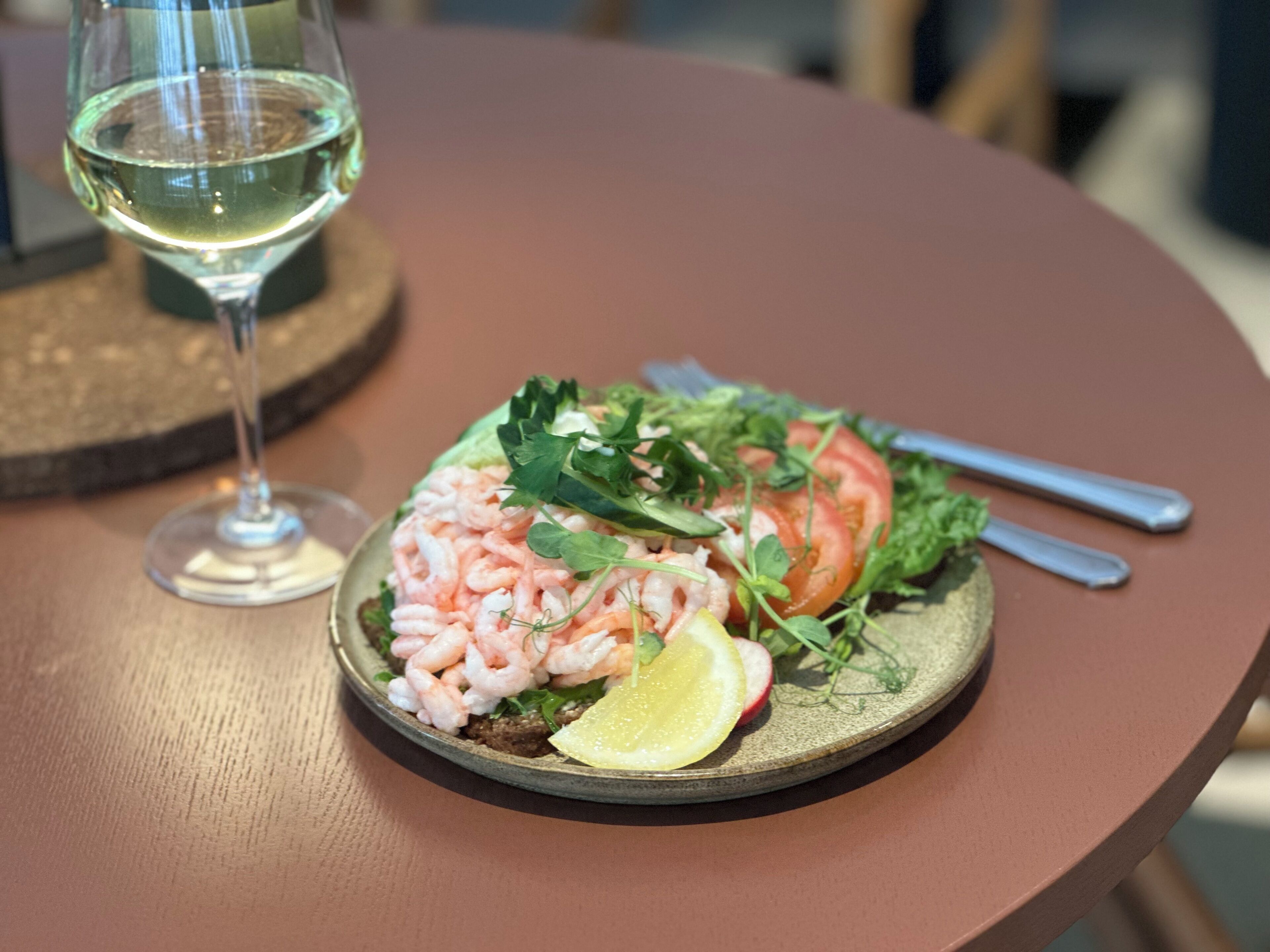 A plate of shrimp salad with a lemon wedge and a glass of white wine on a round table.