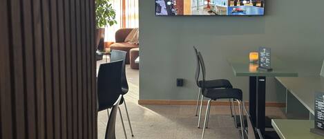 Un vestíbulo de hotel con un gran panel que muestra diversas comodidades, como una terraza, recepción, desayuno, gimnasio, sauna/relajación y sala de juegos.