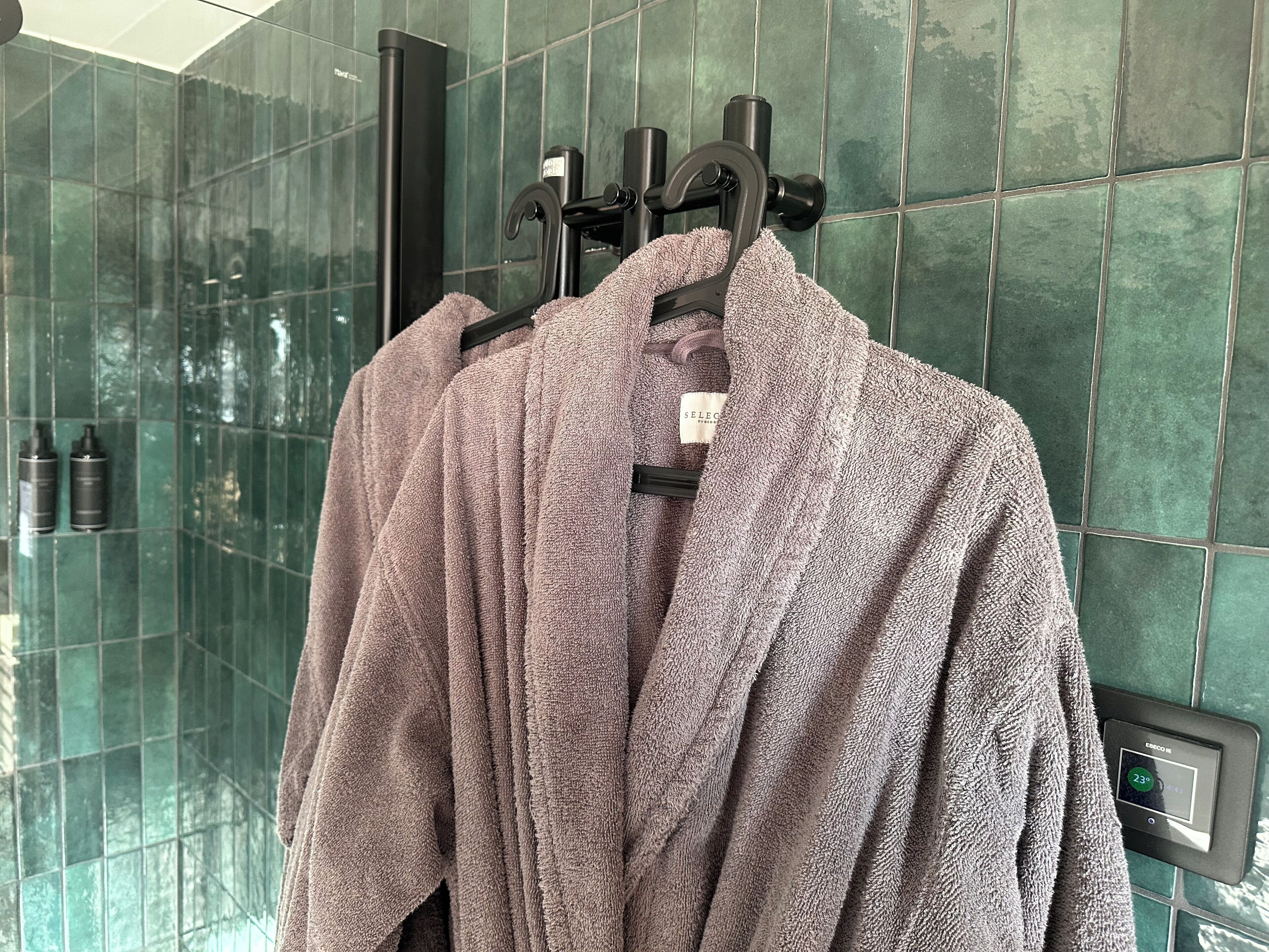A bathroom with a glass shower enclosure, a towel rack with two towels, and a digital thermostat on the wall.