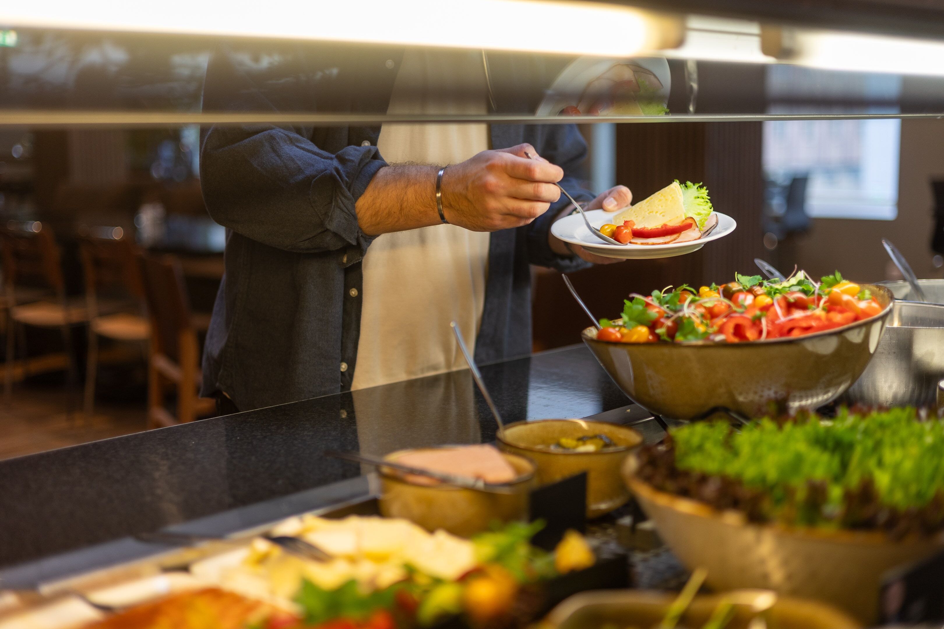 A buffet setup with various food items and a person serving themselves.