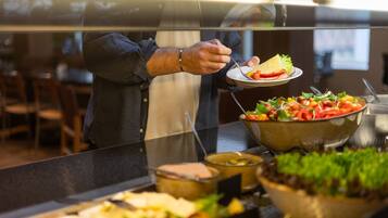 A buffet setup with various food items and a person serving themselves.
