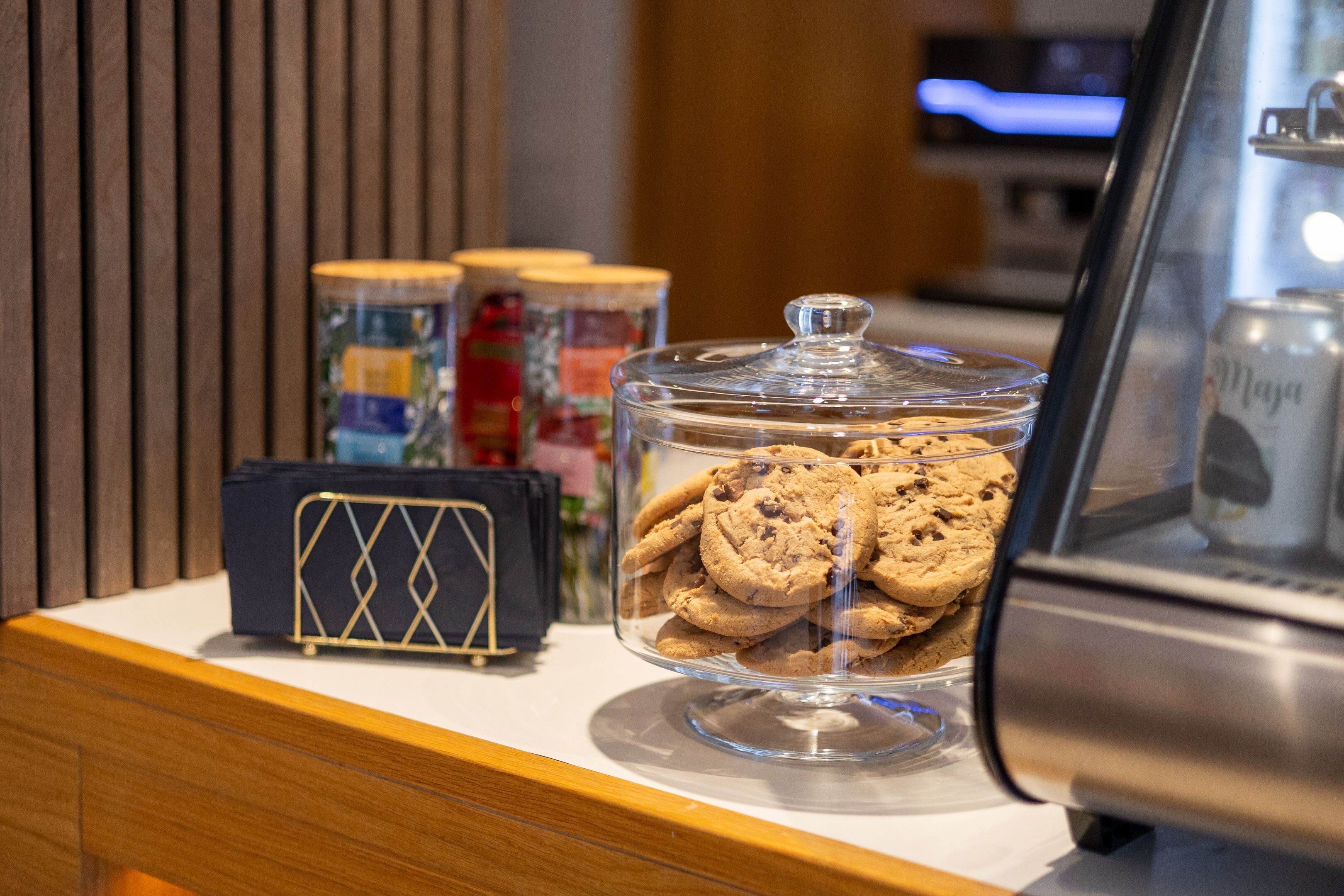 Una exposición de galletas en un tarro de vidrio con tapa, una pequeña bolsa negra y frascos de condimentos sobre una encimera.