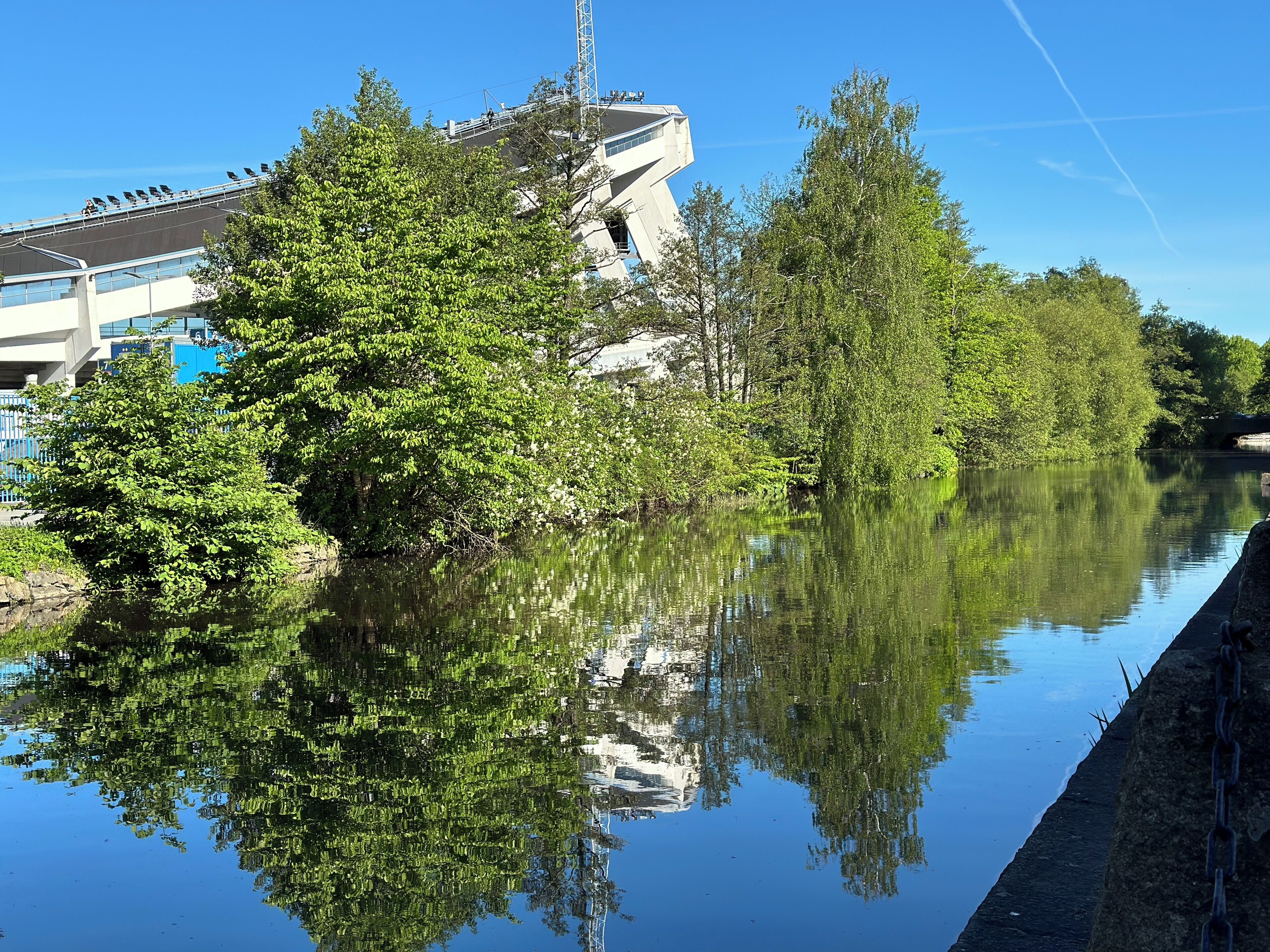 Un río tranquilo que refleja árboles y un edificio moderno con una arquitectura singular.