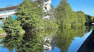 Un río tranquilo que refleja árboles y un edificio moderno con una arquitectura singular.