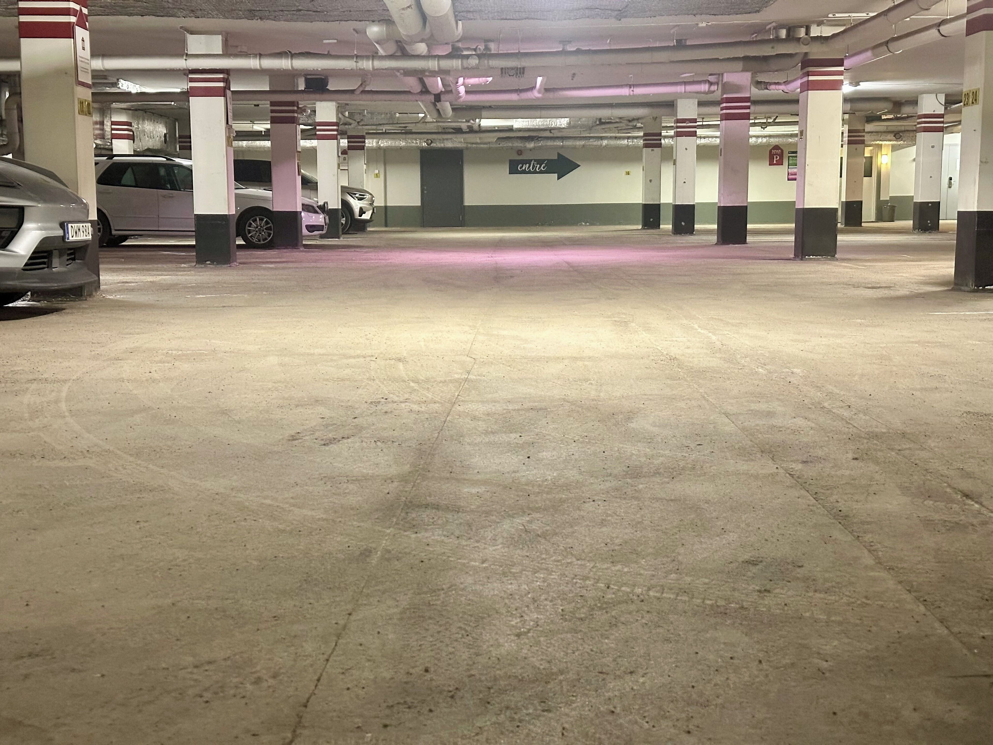 A multi-level parking garage with concrete floors and pillars, an arrow sign indicating the entrance, and several parked cars.