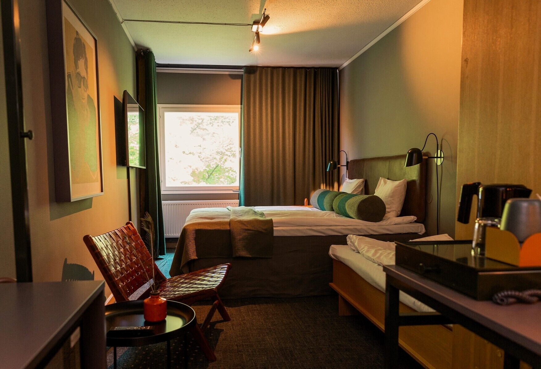 A hotel room with a bed, a desk, a chair, a small table, and a window with curtains.