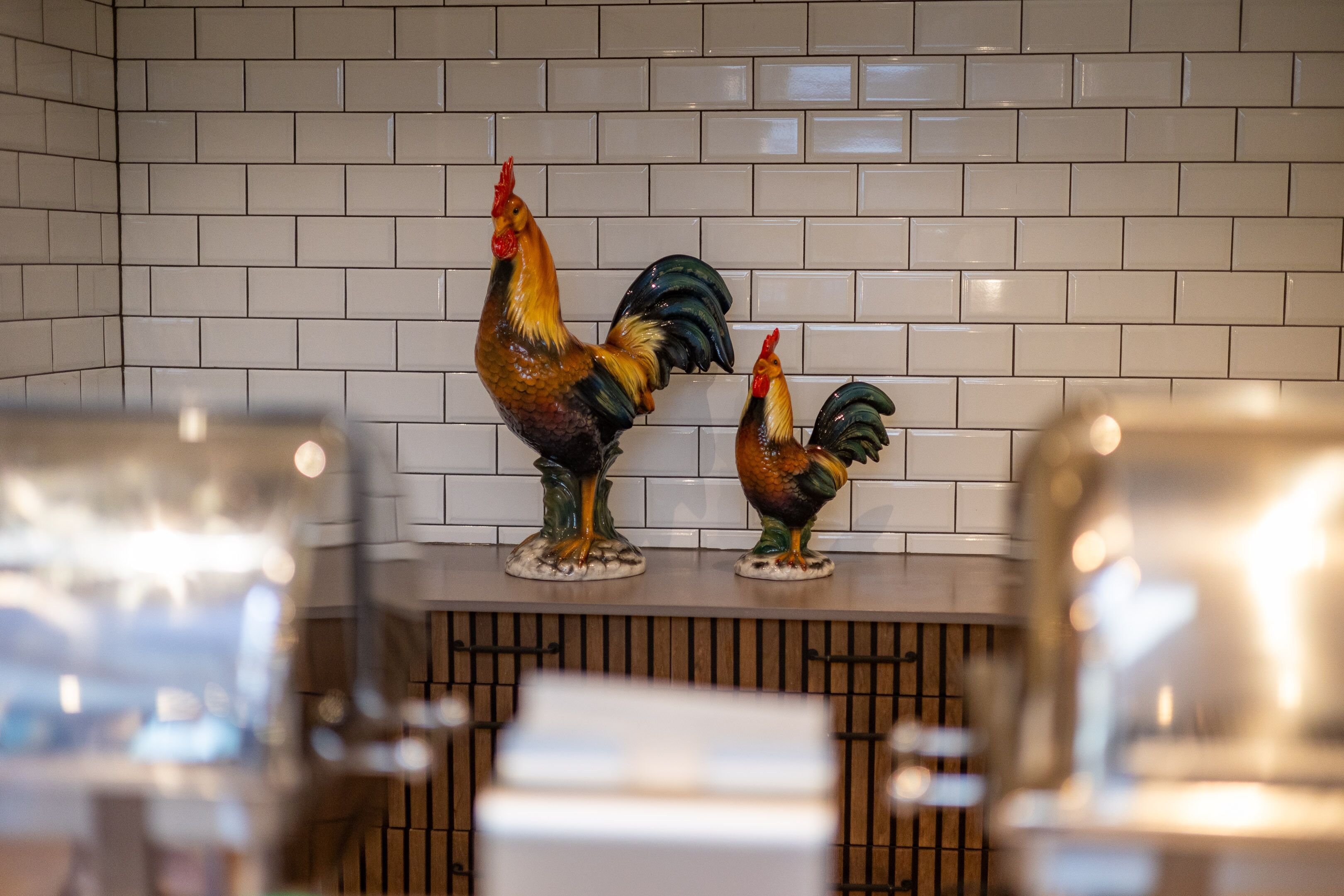 A kitchen with white tiled backsplash and two ceramic roosters on the counter.